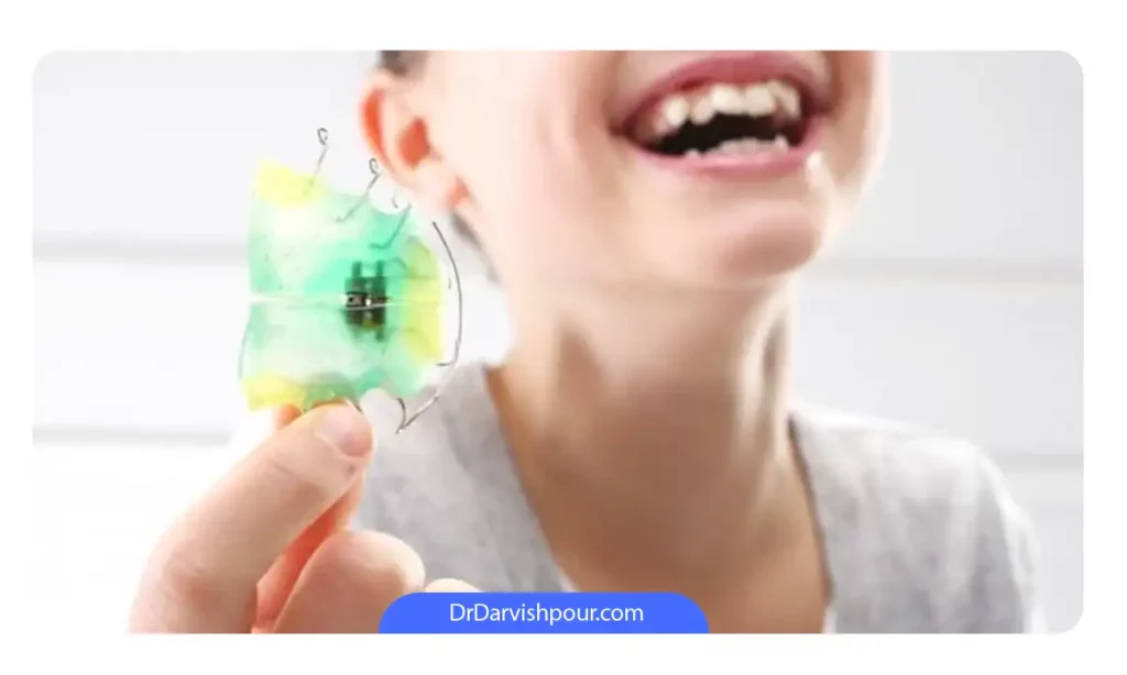 کودکی که یک وسیله ارتودنسی پیشگیری در دست دارد و در حال خندیدن است